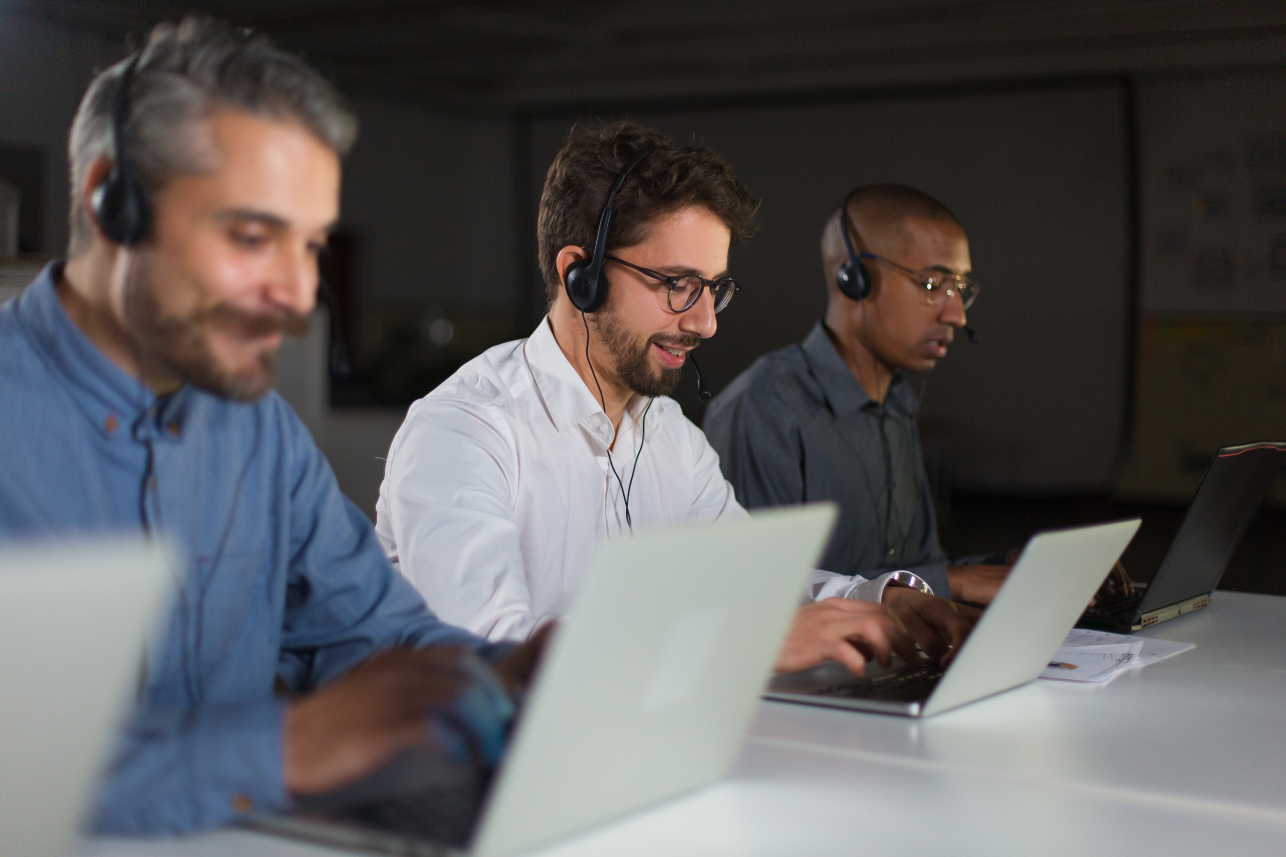 Three support staff wearing headsets working on laptops in office.