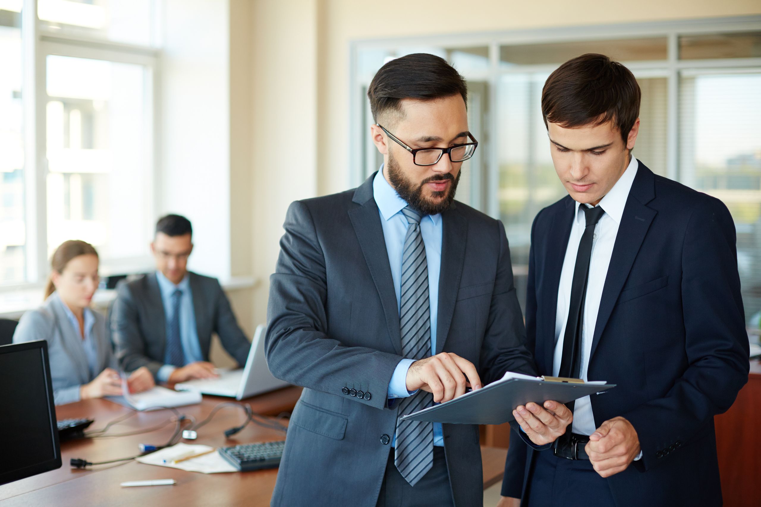 Two people in suits having discussion while looking at clipboard. Two people in suits having discussion while looking at clipboard.